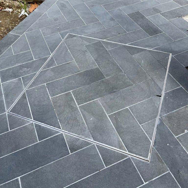 HIDE stainless steel Manhole Cover with grey herringbone paving pattern inlay.