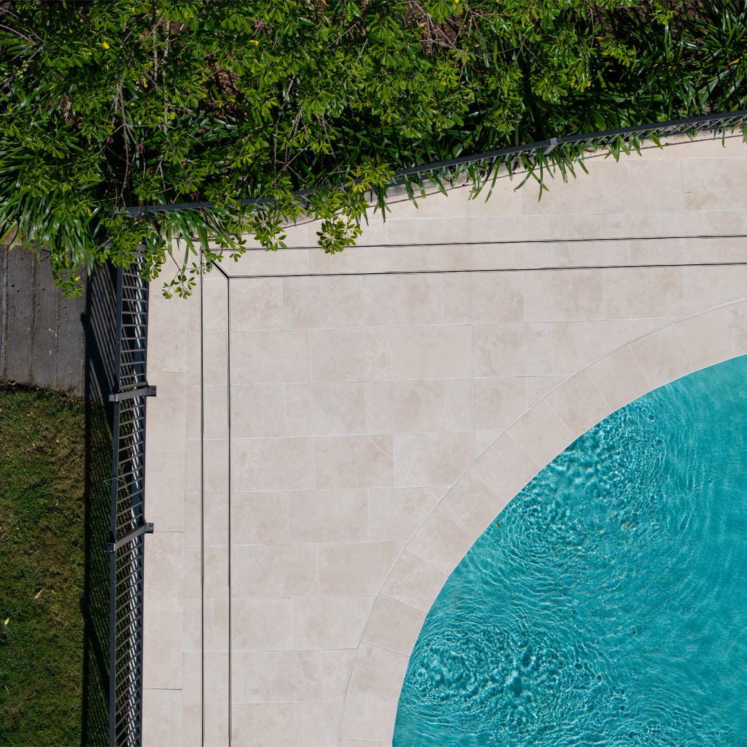 Stainless steel HIDE Linear Strip Drain Cover with grey tile inlay installed next to swimming pool.