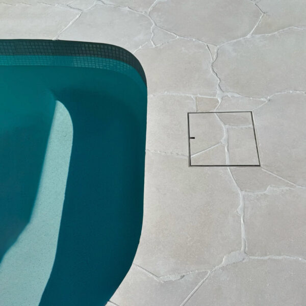 HIDE inlay Skimmer Lid set flush into light crazy pave tiling, continuing the crazy pave pattern through the Cover for a seamless finish.