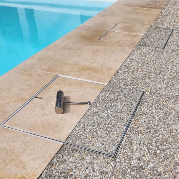 Two stainless steel HIDE Skimmer Lids installed with tile coping and exposed aggregate concrete dual inlay next to swimming pool.